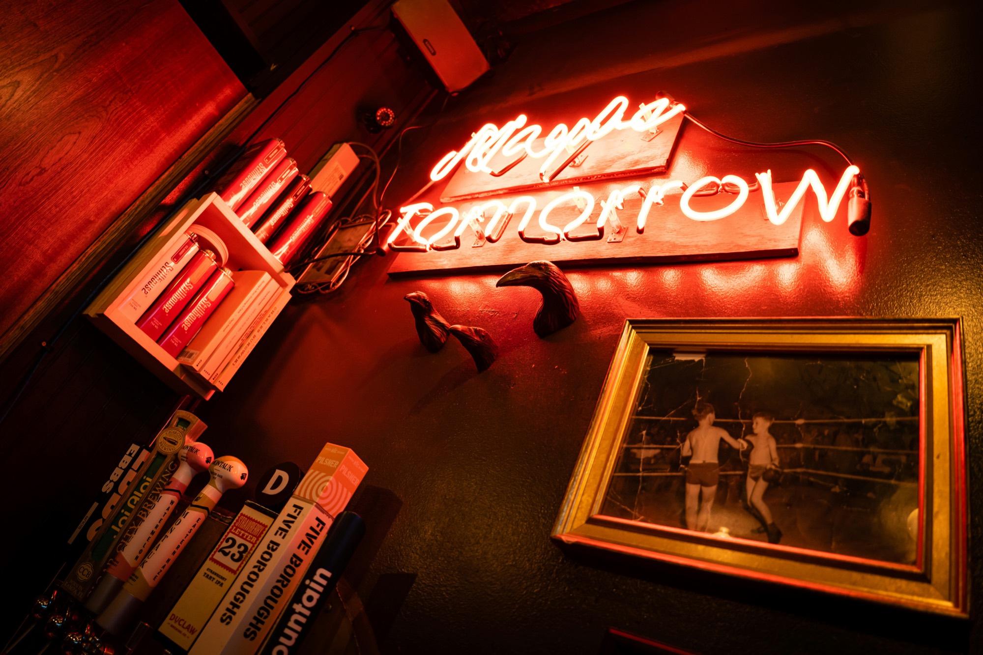 A red neon sign reading 'Maybe Tomorrow' over a framed old boxing photo and a row of tap handles.