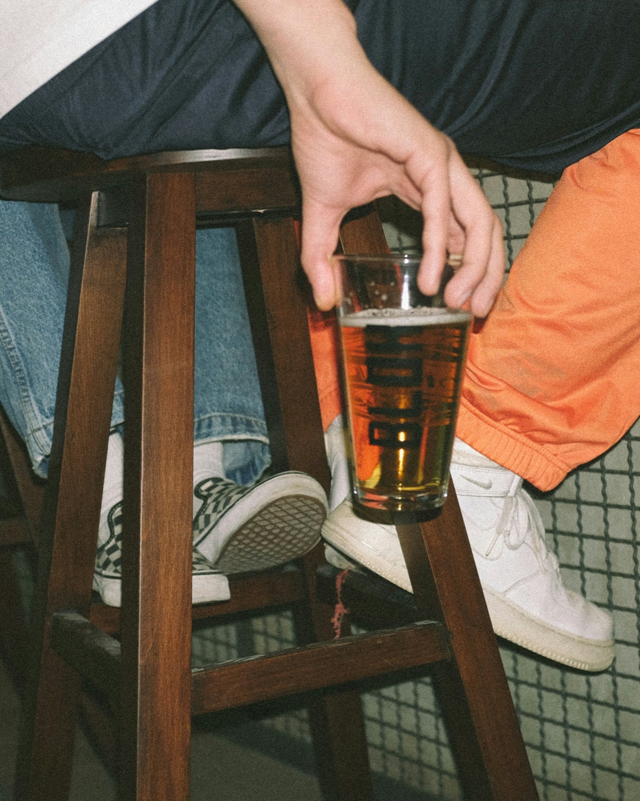Flash photo: two regulars side by side on a wooden bar stool, one holding a pint.